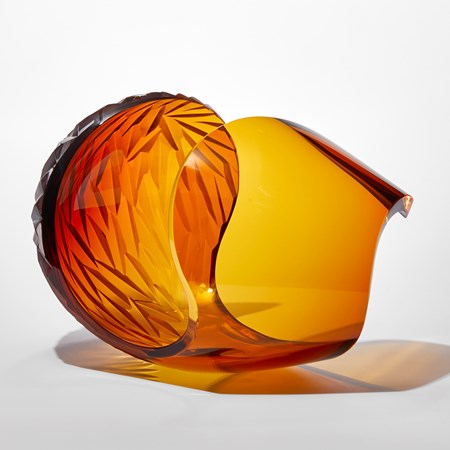 transparent dark rich amber laid down egg shaped sculpture with large cut away section leaving a sweeping curved edge with repeat diamond pattern cut area hand made from glass