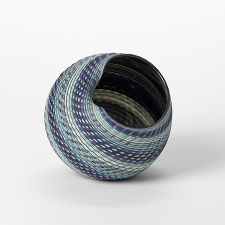 round vessel with offset wide opening with meandering rim with matt textured exterior and glossy interior with bands of colours in blue jade indigo cream and white hand made from glass