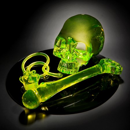 neon green coloured art glass sculpture of skull and bone on black mirror base