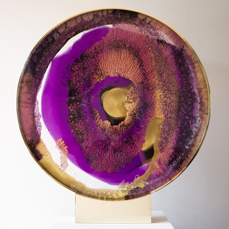 round glass art sculpture in deep purple yellow and brown resembling pattern of an eyeball