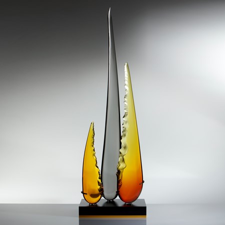 a trio of glass shards one long carbon coloured and centre flanked by two shorter amber and yellow shards resting on black metal base