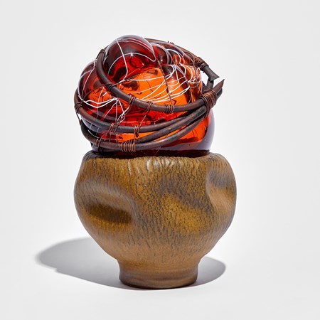 ochre leathery looking rustic ceramic bowl containing a red/orange mass of glass with white lines bound in copper pipe