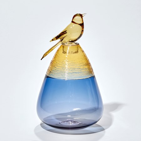 blue and yellow gold vessel with smooth transparent base with woven top detail and stopper adorned with a golden bird handblown from glass