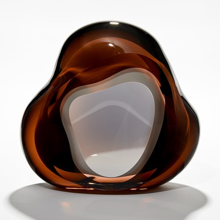 amorphous sculpture in layers of transparent rich dark brown and intense amber with central organic hole in the middle lined in opaque white hand made from glass