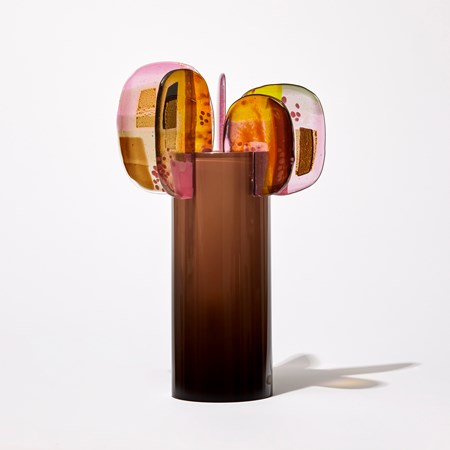 aubergine brown fading to the top opaque cylinder with five rounded panels of abstractly pattern glass in pink yellow gold and brown perched on the rim hand made from glass
