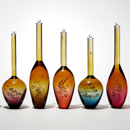 installation of seven transparent solid bottles in a row with spiral helix detail trapped within each with a long thin neck and bulbous base fading from amber at the top to various colours at the base hand made from glass
