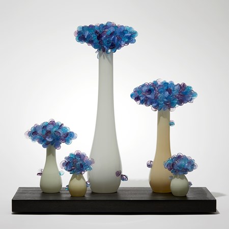 rectangular black wooden base with bonsai inspired trees set on its top each with bulbous rounded bases and clusters of lollipop shaped various blue and purple leaves hand made from glass