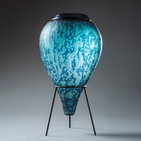 inverted teardrop vessel in mixed aquas and blues with soft mottled organic surface texture and pattern with top opening with smooth black rim hand made from glass with black steel tripod stand