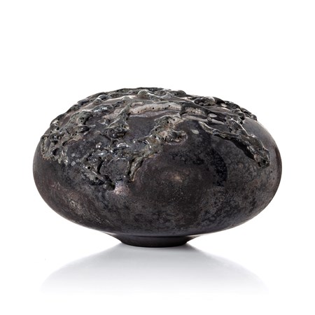 black rounded low mushroom shaped sculpture with leathery weathered surface covered in organic raised surface texture with a dark metallic sheen hand made from glass