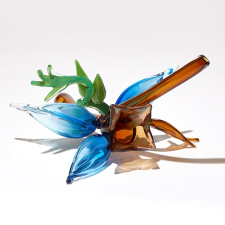 abstract plant inspired sculpture with transparent tobacco coloured stem with a cluster of bright blue buds brown bell shaped flower and bright green tendrils hand made from glass