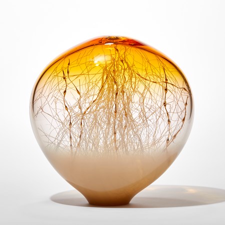 round transparent abstract glass sculpture with soft opaque fading light bronze base and golden yellow top  with clear middle trapped inside are a multitude of criss crossing thin white canes some with bulbous sections that are gold