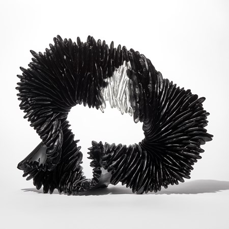 black ridged and textured standing glass sculpture with the appearance of a loop unravelling ribbon with one small clear upper wedged section