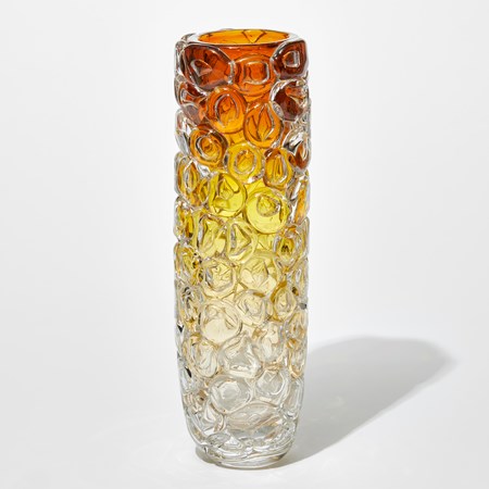 tall round column shaped transparent vase with the outer surface covered in oversized squashed bubbles with clear base fading to soft gold then rich gold and dark amber at the top hand made from glass
