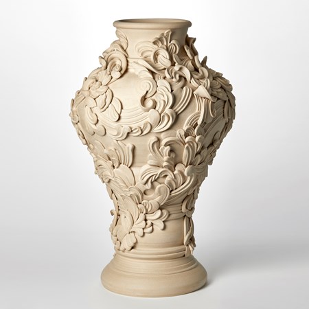 tall classical sandstone coloured vase with narrowing base bulging upper middle and top narrower round opening covered with architectural rococo swirls and flourishes hand made from white st thomas clay  
