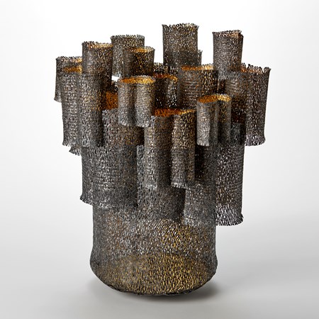 large organically perforated tubular form with a multitude of smaller tubes stacked on top of and slotted into it and on each other with a dark matt brown exterior and gold interior hand made from steel and twenty four carat gold leaf