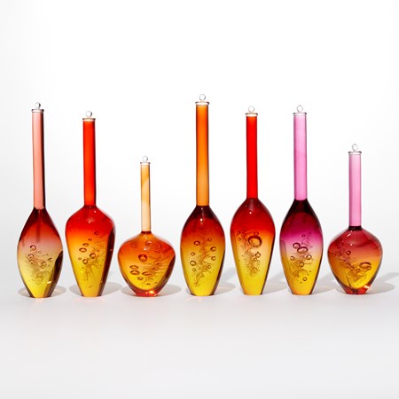 set of seven solid transparent glass bottles with a helix of bubbles trapped inside gold bottom halves red and pink top halves each with a long neck and stopper on the top