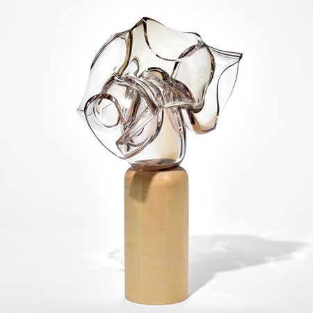 sleek column of birch wood with soft rounded top edge holding aloft a stacked mass of transparent collapsing and deflating bubble forms with a tint of bronze and pink hand made from blown glass
