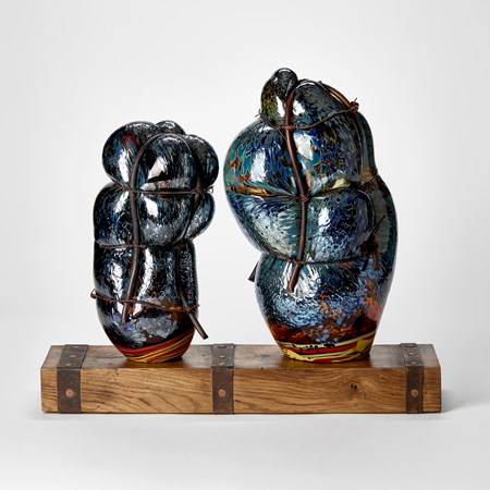 wooden rustic base with ages metal straps dividing the surface into two areas with two abstract simplified figures standing on the top hand made from glass and each bound in copper pipe representing a mother and child