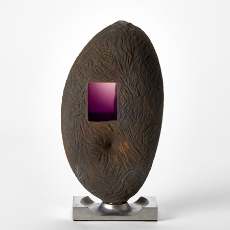 tall ovoid with rough scratched and incised surface with a dark metallic finish with a small transparent purple rectangular window revealing the interior perched above a solid steel base with circular recess with the two held together by a magnet hand made from glass