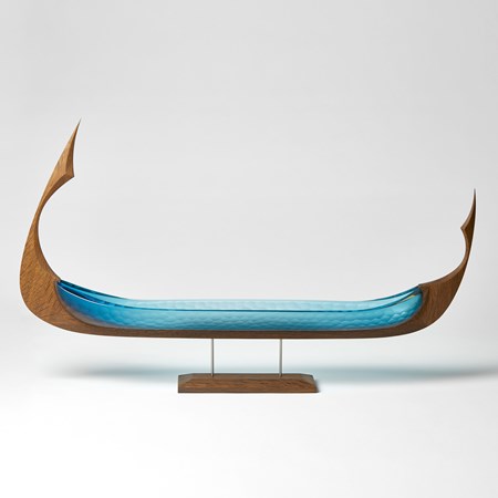 stylised viking ship with a keel made of oak and the hull from steel blue glass with a scalloped cut surface pattern raised on a simple stand