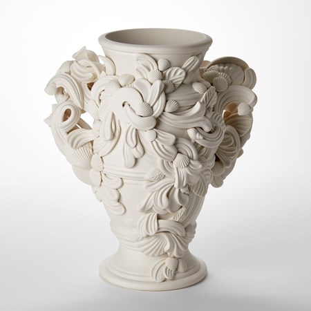 hand thrown and sculpted porcelain vessel with elegant round flared foot and top wide opening with bulging barrel shaped middle with two large handles on either side with the entire piece covered in organic rococo swirls shells and leaves 