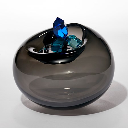 transparent dark grey round bubble with soft top opening cradling a stacked cluster of vibrantly coloured cut gems in blue jade turquoise emerald and amber hand made from blown and cut glass