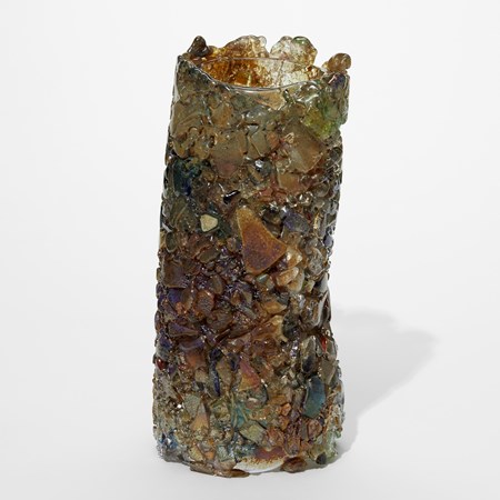 leaning soft tubular vase in rust brown dark green and various metallic neutral tones with the surface covered is crushed and molten flat shards all squashed together to cover the surface creating an organic irregular top rim hand made from glass