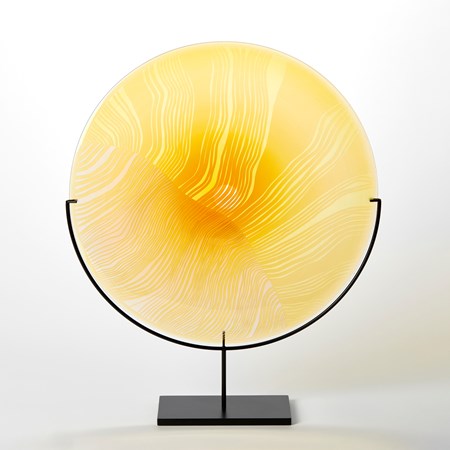round yellow disc with surface cut abstract lines and patterns mounted on a matt black stand hand made from glass