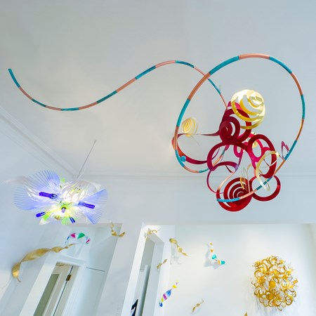 red gold aqua and copper hanging sculpture consisting of a mass of swirls curls and spirals created from flat sheet metal and twisted into three dimensional forms created from hand-painted copper, oxydyed aluminium & brass with a long trailing striped tail like a kite