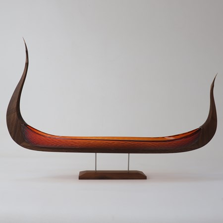 simple and stylish artwork based on a viking ship with keel made of fumed oak and hull of red orange blown glass with a repeat pattern cut into the surface displayed raised on a simple stand
