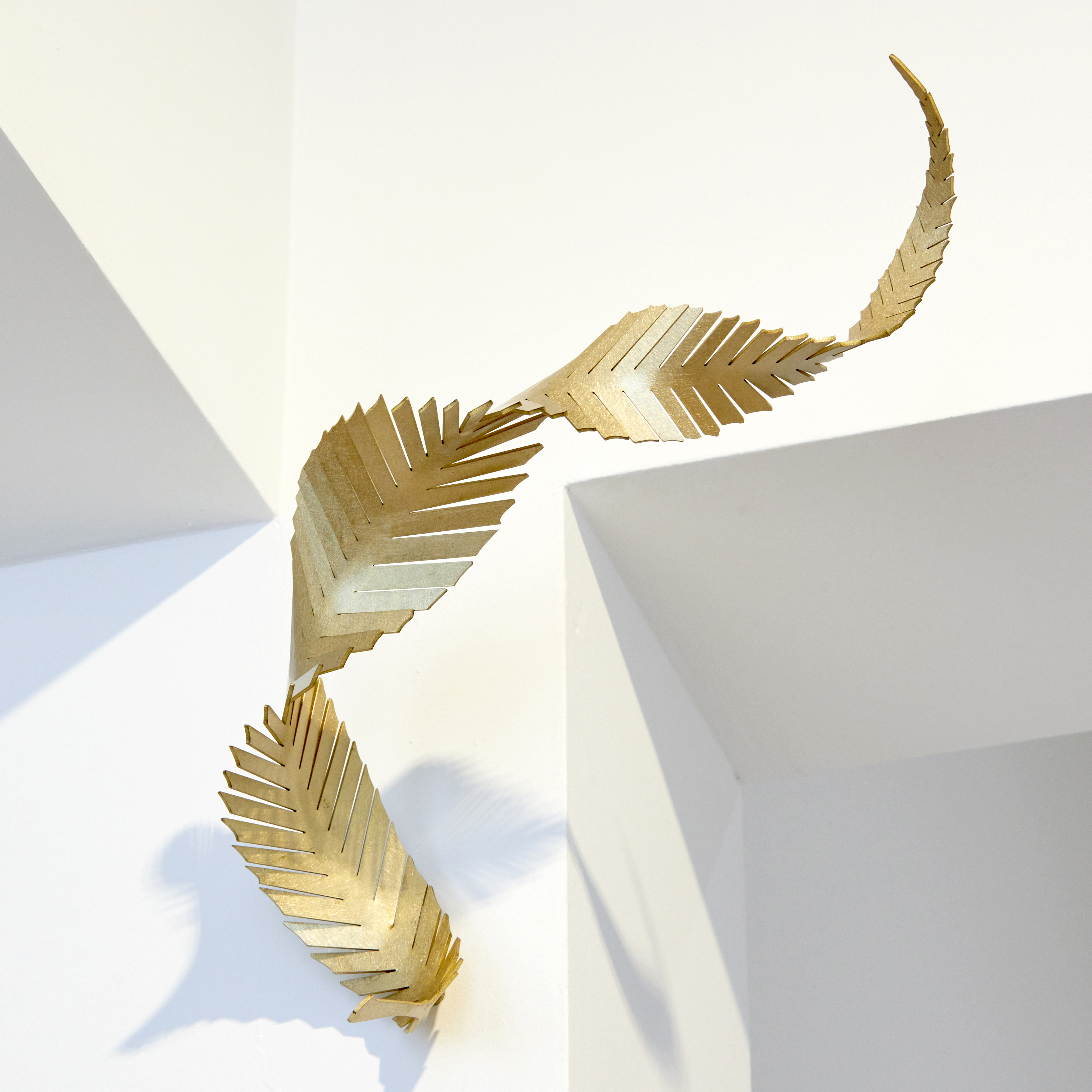 abstract angular curling feather with straight slits along the length and curling twisting form with a brushed finish and wall mounted as it just touching the surface