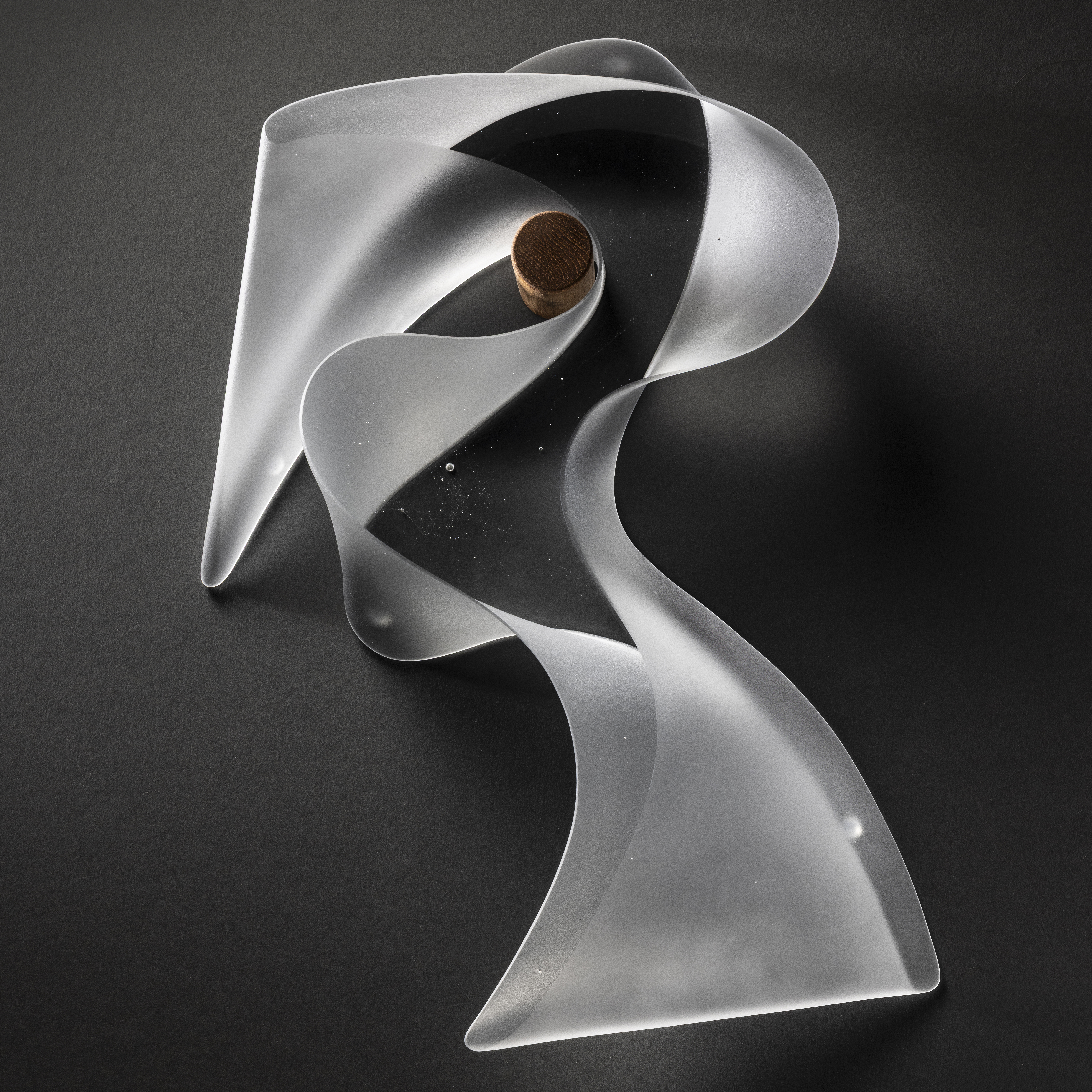 transparent abstract sculpture with the appearance of chunky curling calligraphy with a clear front and back and a meandering opaque frosted side edge that follows the form hand made from cast glass and hing on the wall by a stout teak peg