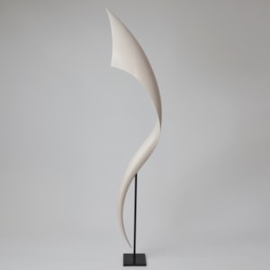 tall standing curved flaring white wooden sculpture with narrow base widening towards to the top and as it curves around presented on a black steel simple stand