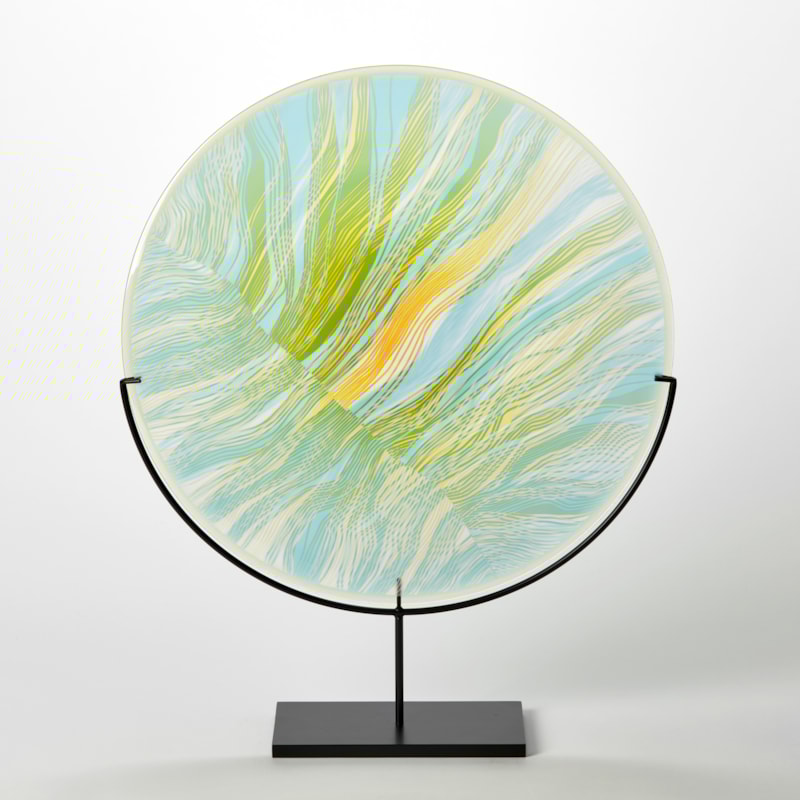translucent green yellow and aqua round disc on a matt black stand with abstract cut lines on the surface hand made from glass