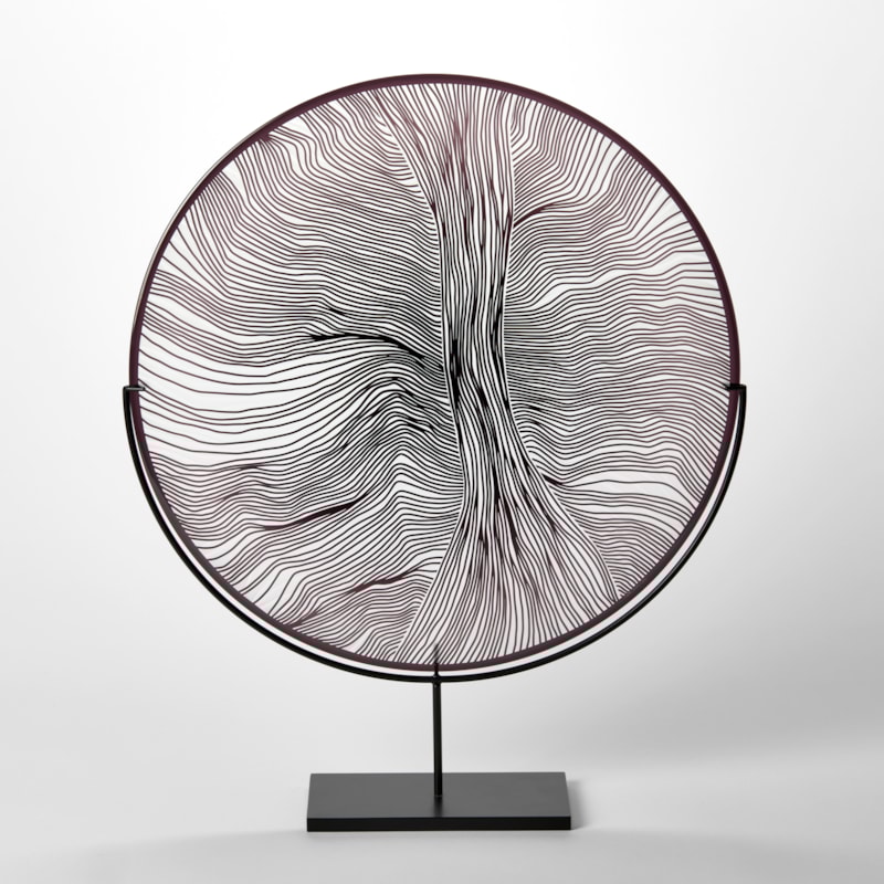 round plate in clear and black with cut abstract surface linear patterns hand made from glass held aloft on a steel matt black stand