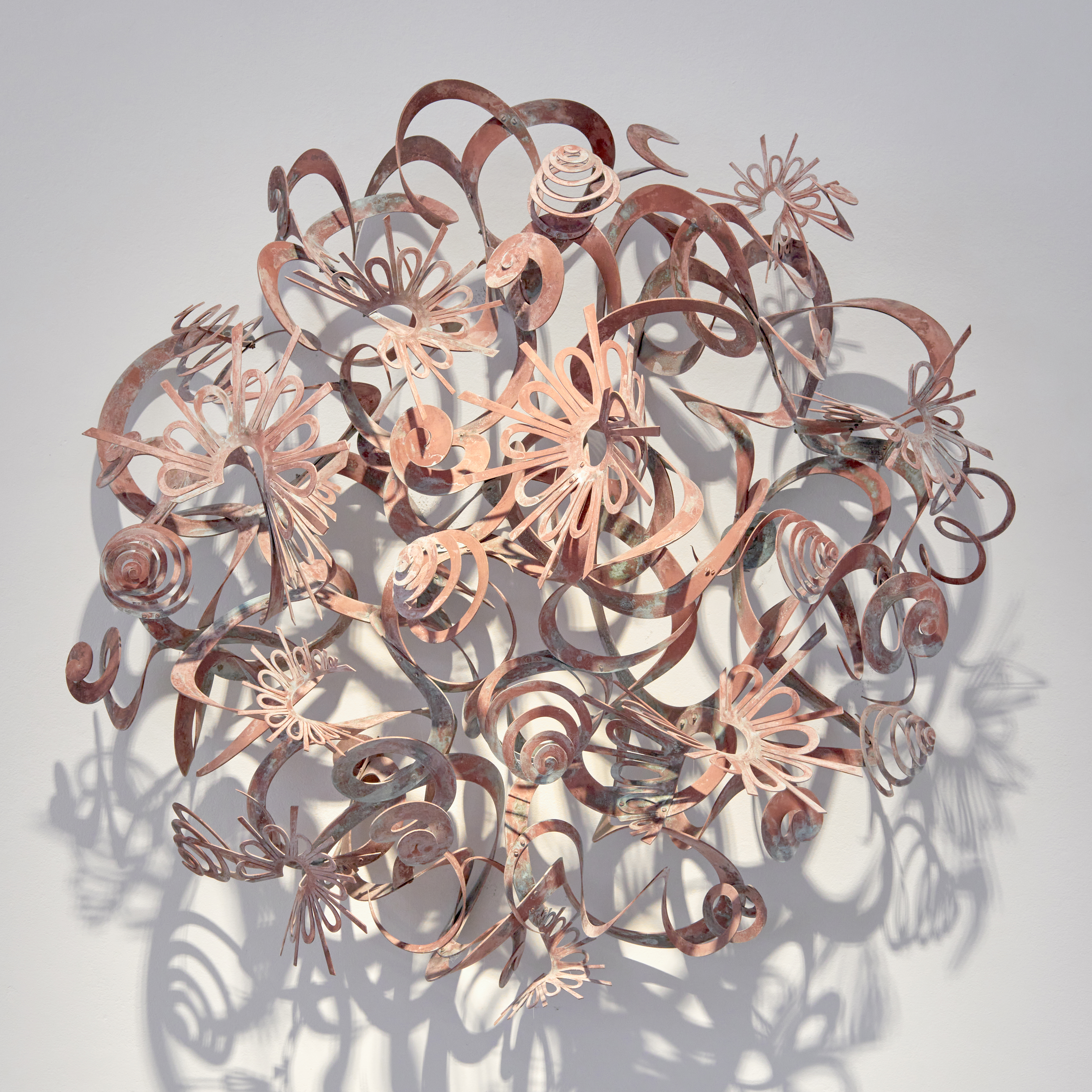 sun inspired wall hung artwork made from patinated brass consisting of swirls spirals curls and shapes that emerge from the wall