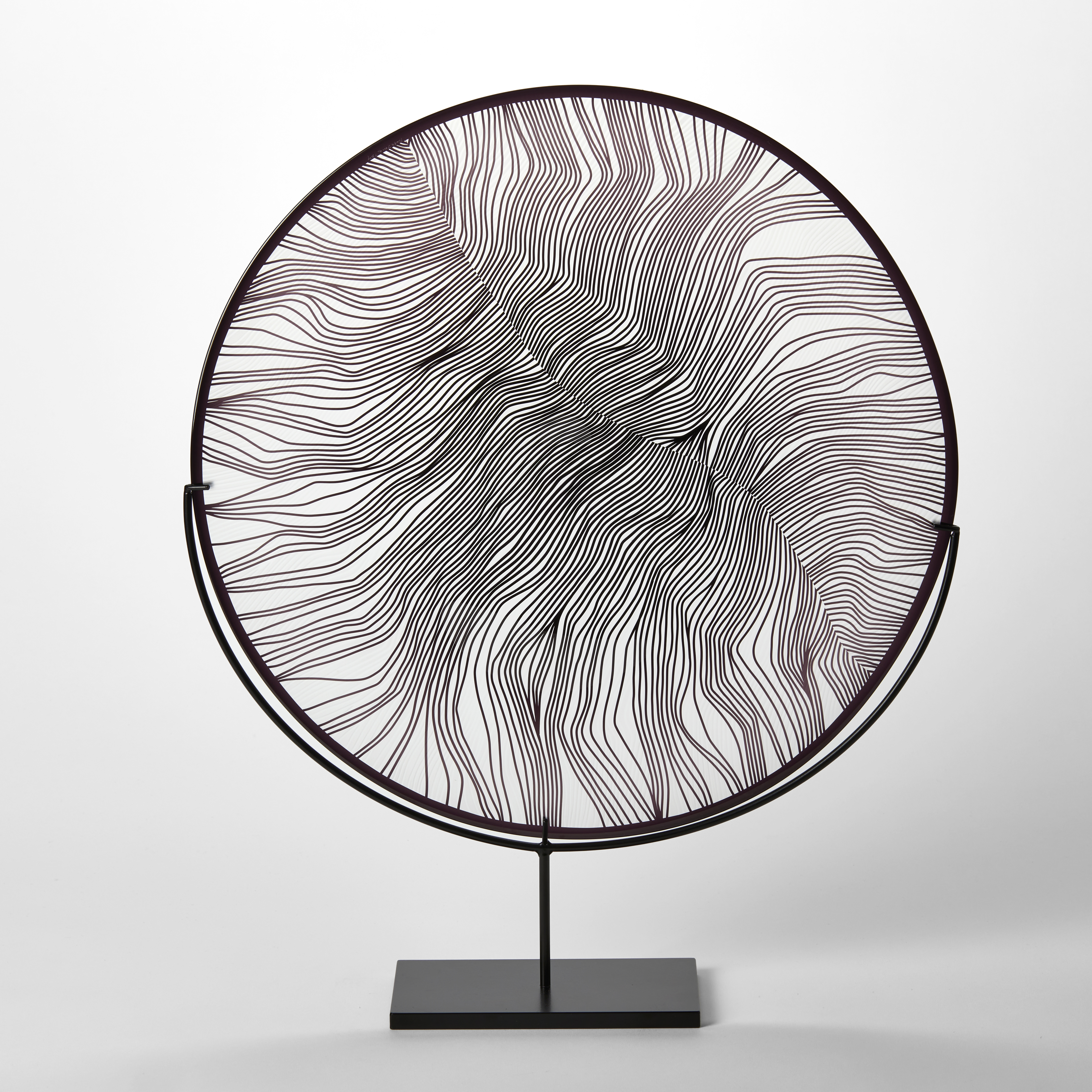 round clear and black glass plate with black rim and cut feather inspired surface pattern hand made and presented on a matt black steel stand 
