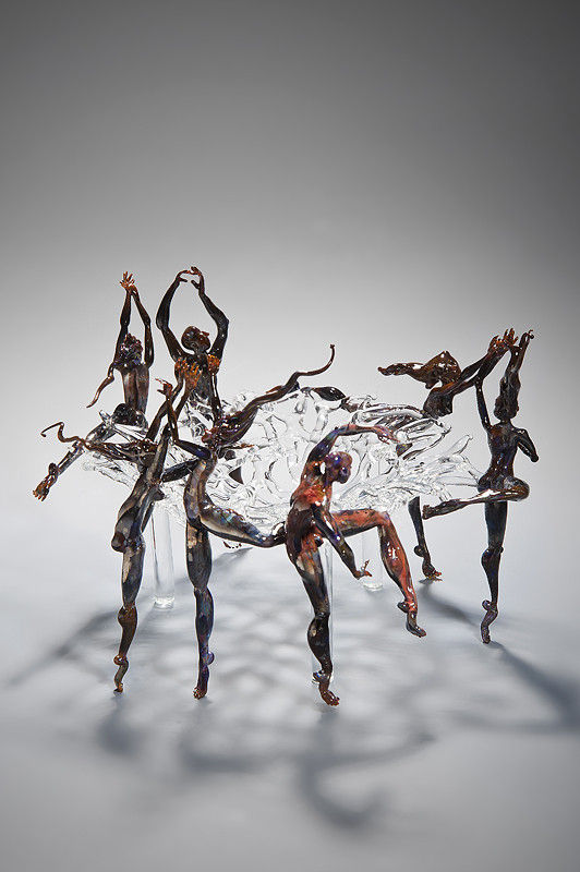 art glass sculpture of figures dancing round central clear glass pane