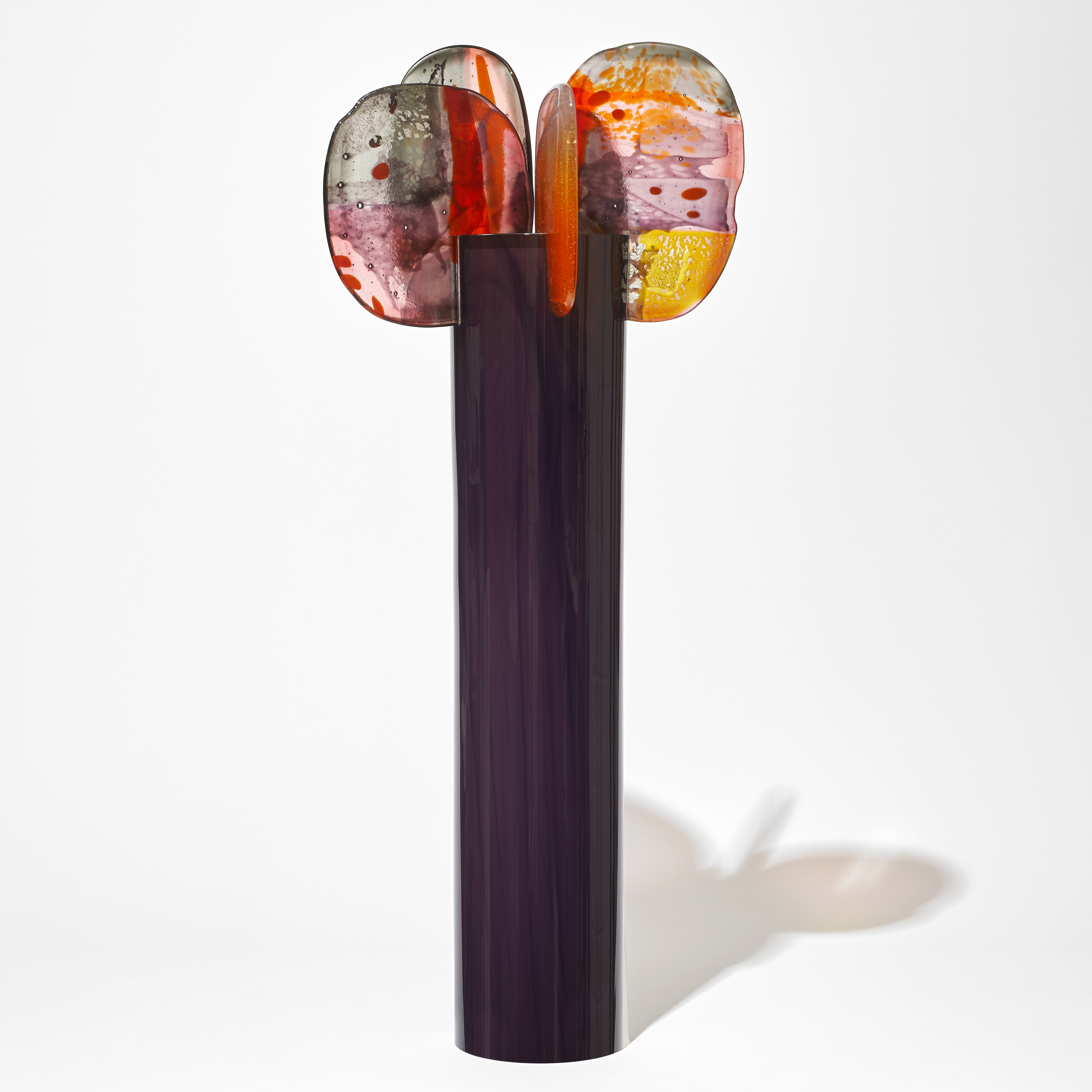 tall opaque shiny rich brown coloured cylinder with 5 rounded finials perched on the top rim in a dazzling array of colours pink yellow red orange and grey with abstract dots and patterns hand made from glass