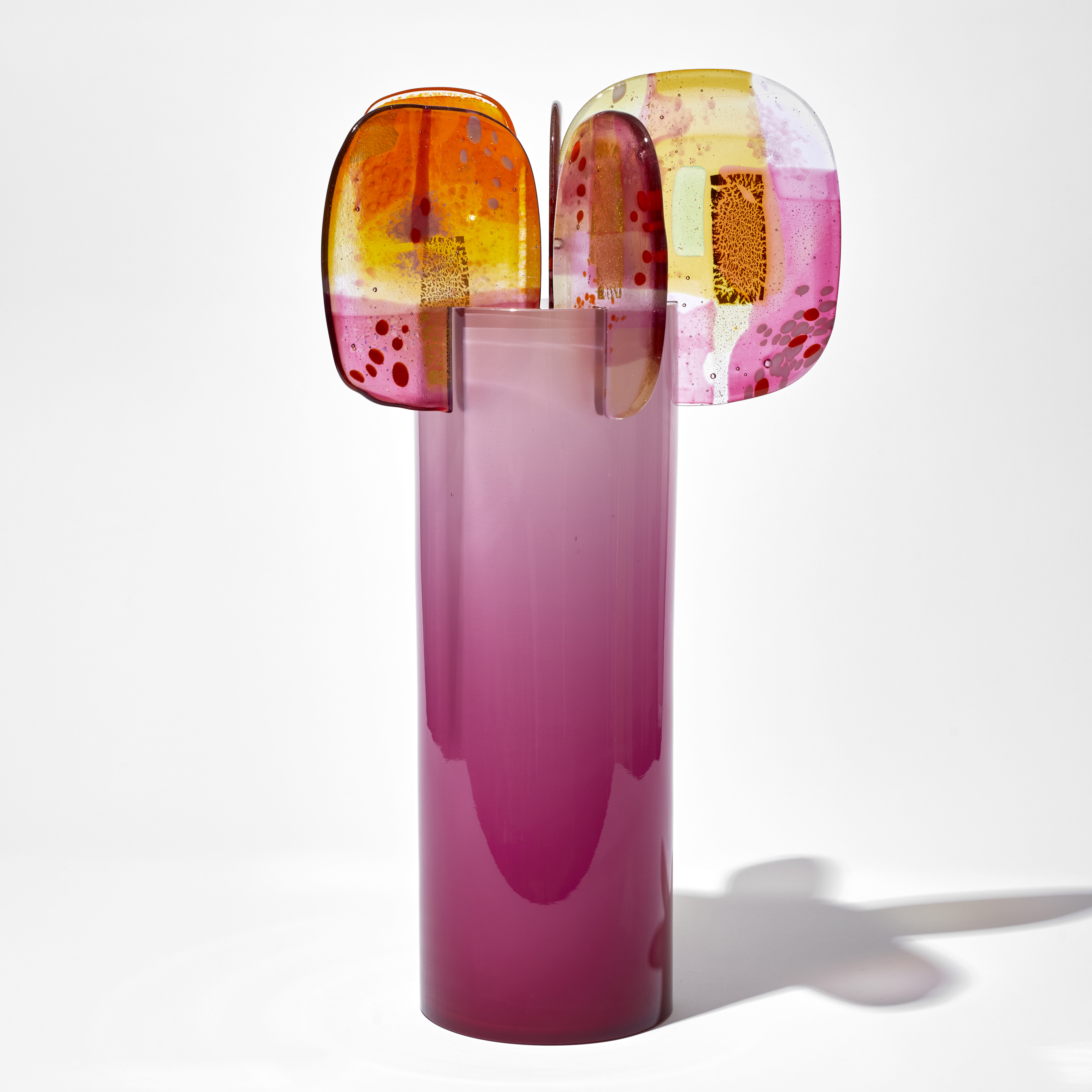 rich shiny opaque pink cylinder with colour fade towards the top with five finials overlapping the top edge each with abstract patterns in pink yellow and gold hand made from blown and fused glass