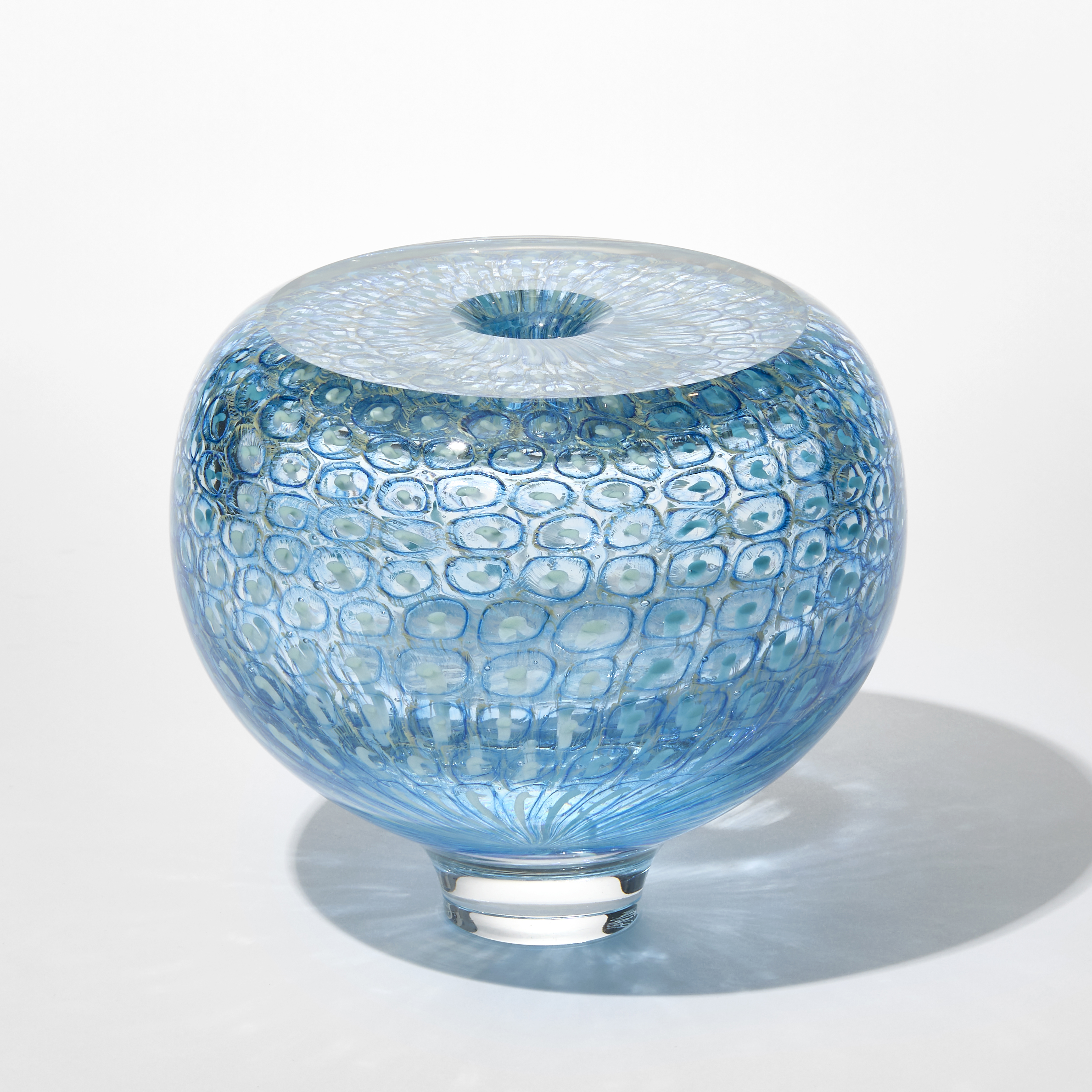 round transparent aquamarine and turquoise vase with incased repeat pattern of rings and dots with a flat shiny top and small central hole hand made from blown glass