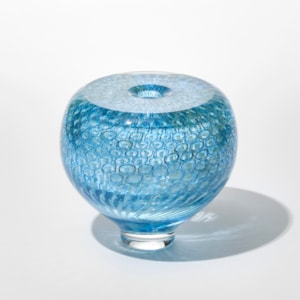 round transparent turquoise vase with repeat circular pattern trapped beneath the surface with flat polished top and small central hole hand blown from glass