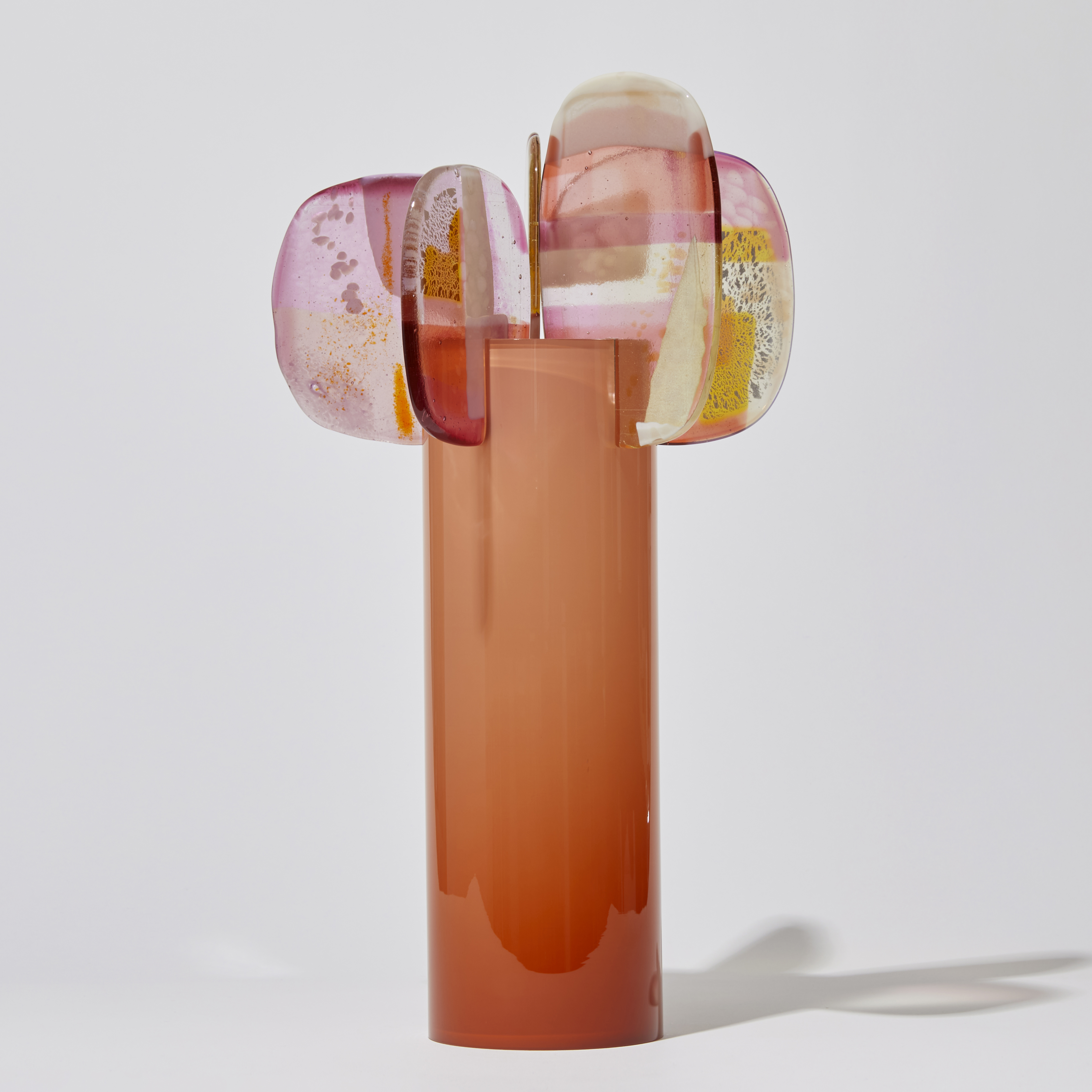 opaque peachy orange cylinder with colour fade from top to bottom and five rounded petals overlapping and perched on the top rim with abstract patterns in pink peach orange yellow white and clear handmade from blown and fused glass
