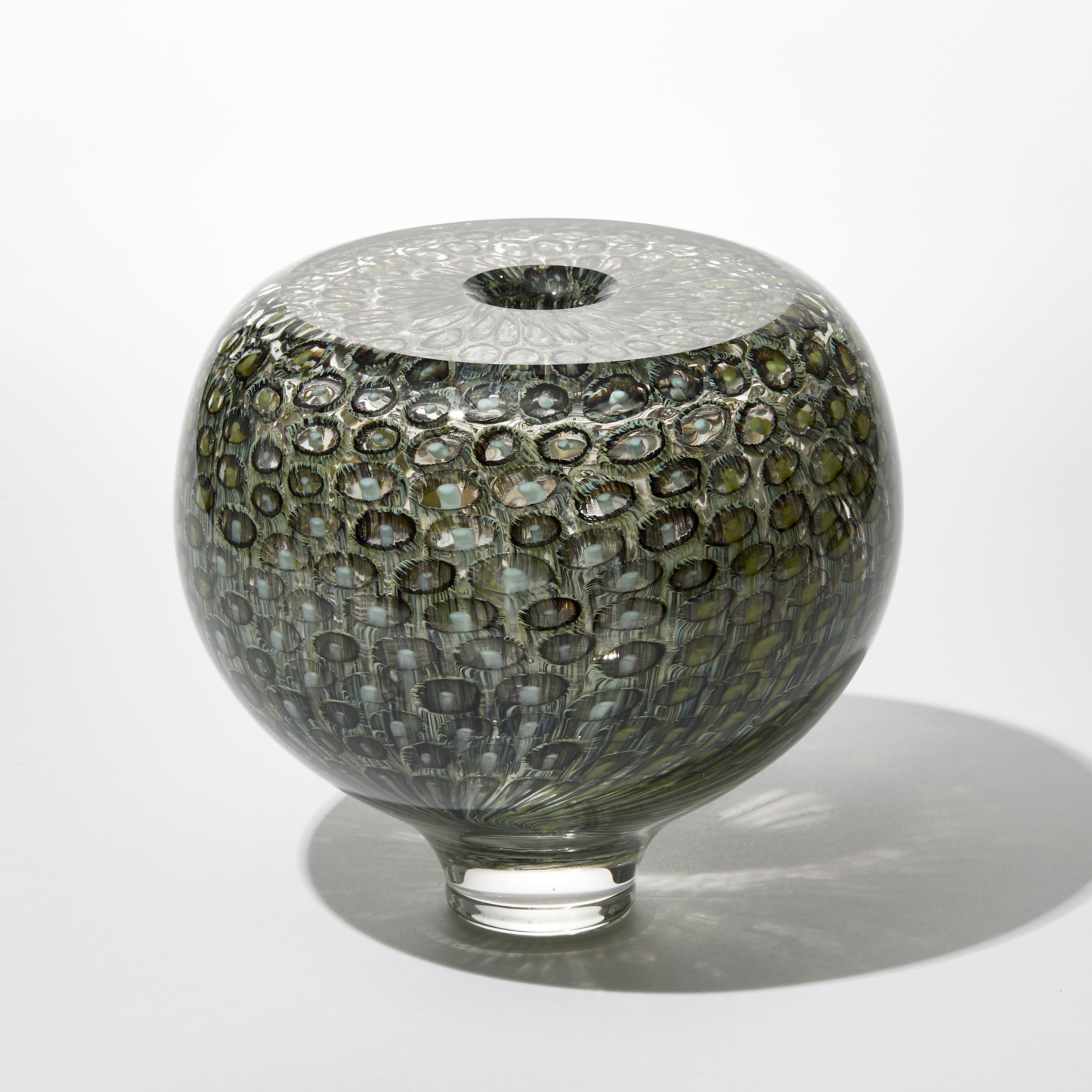 round transparent sea urchin inspired vase with shiny surface and repeat ring and dot pattern trapped within hand made from blown glass