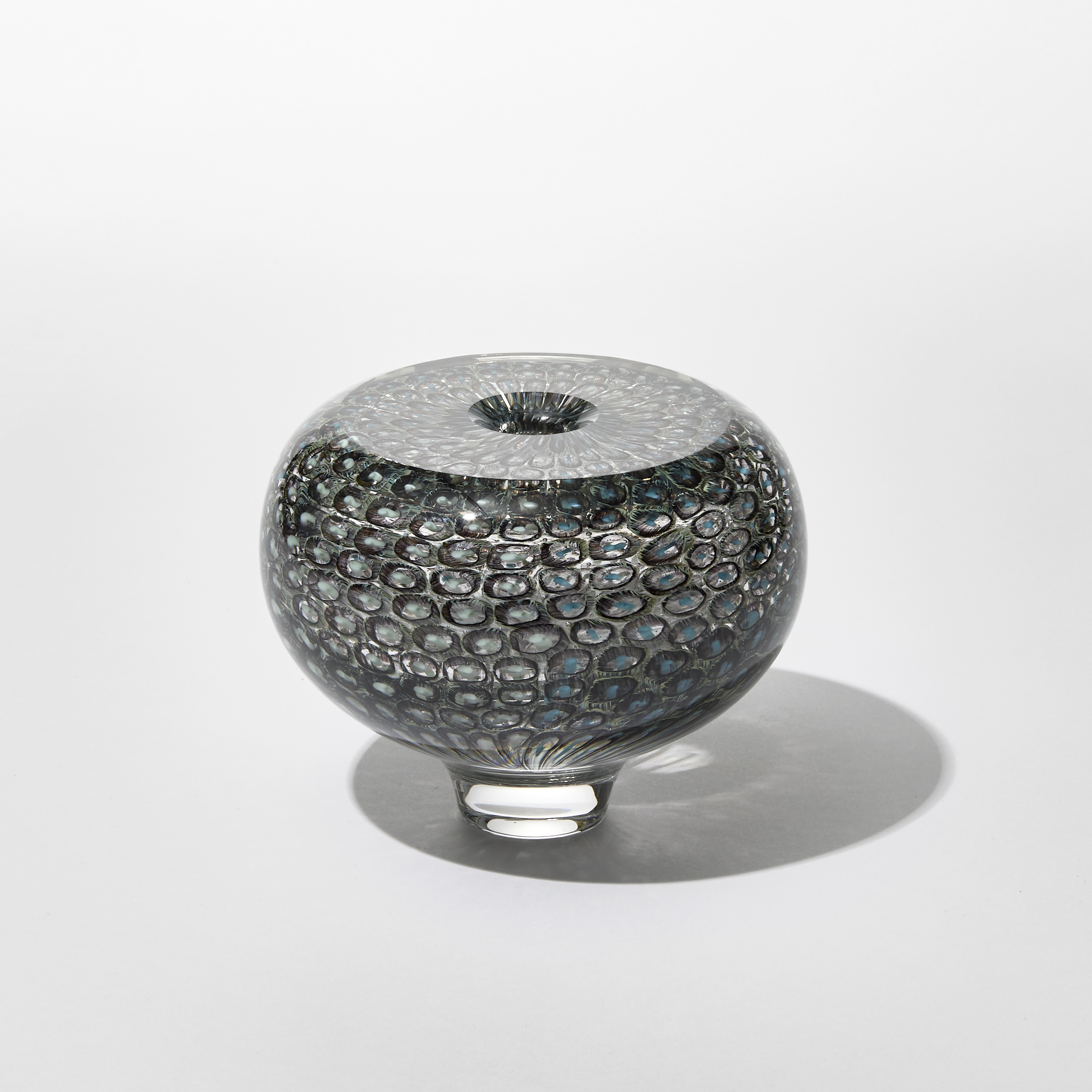 low round transparent vase with incased repeat round small circle and dot pattern in dark green and teal with a flat top surface and small central middle hole hand made from glass