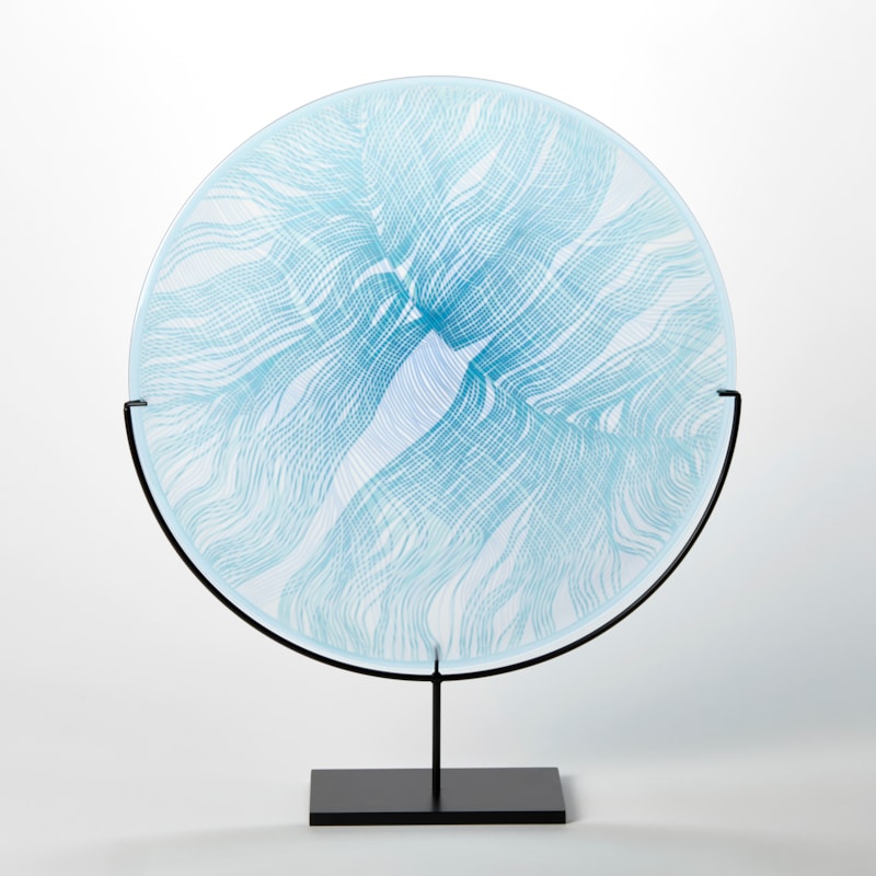 round glass rondel in soft light blue aqua and jade with front cut and etched linear patterns held aloft on a matt black stand