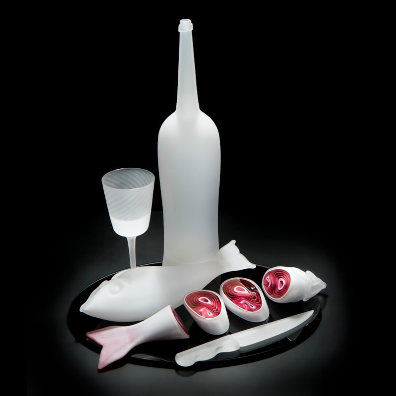 still life blown and sculpted glass art piece of cut fish, knife, bottle and glass in white