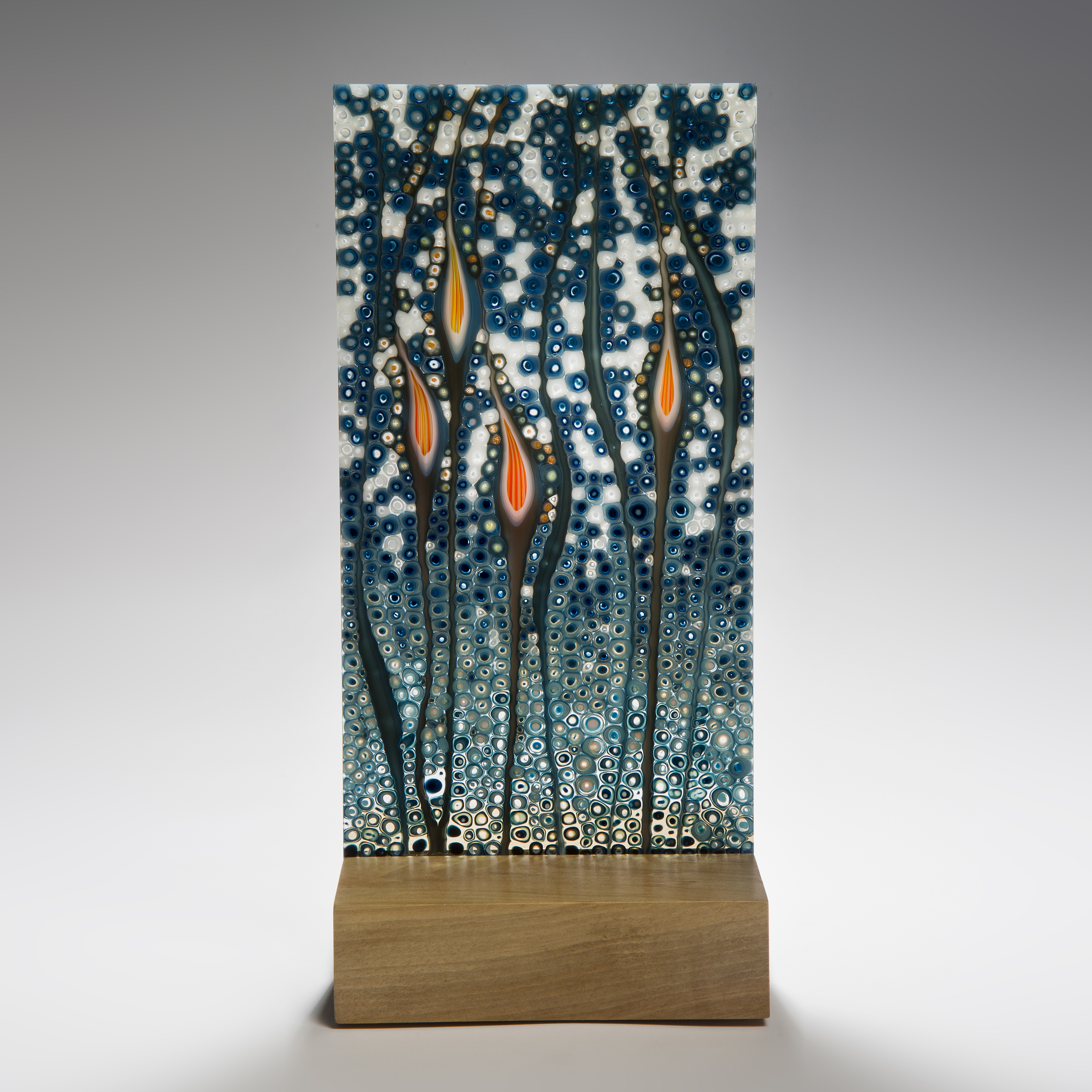 art glass sculptural panel in blue green and orange resting on wooden block