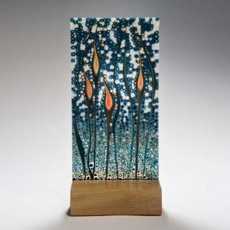 art glass sculptural panel in blue green and orange resting on wooden block