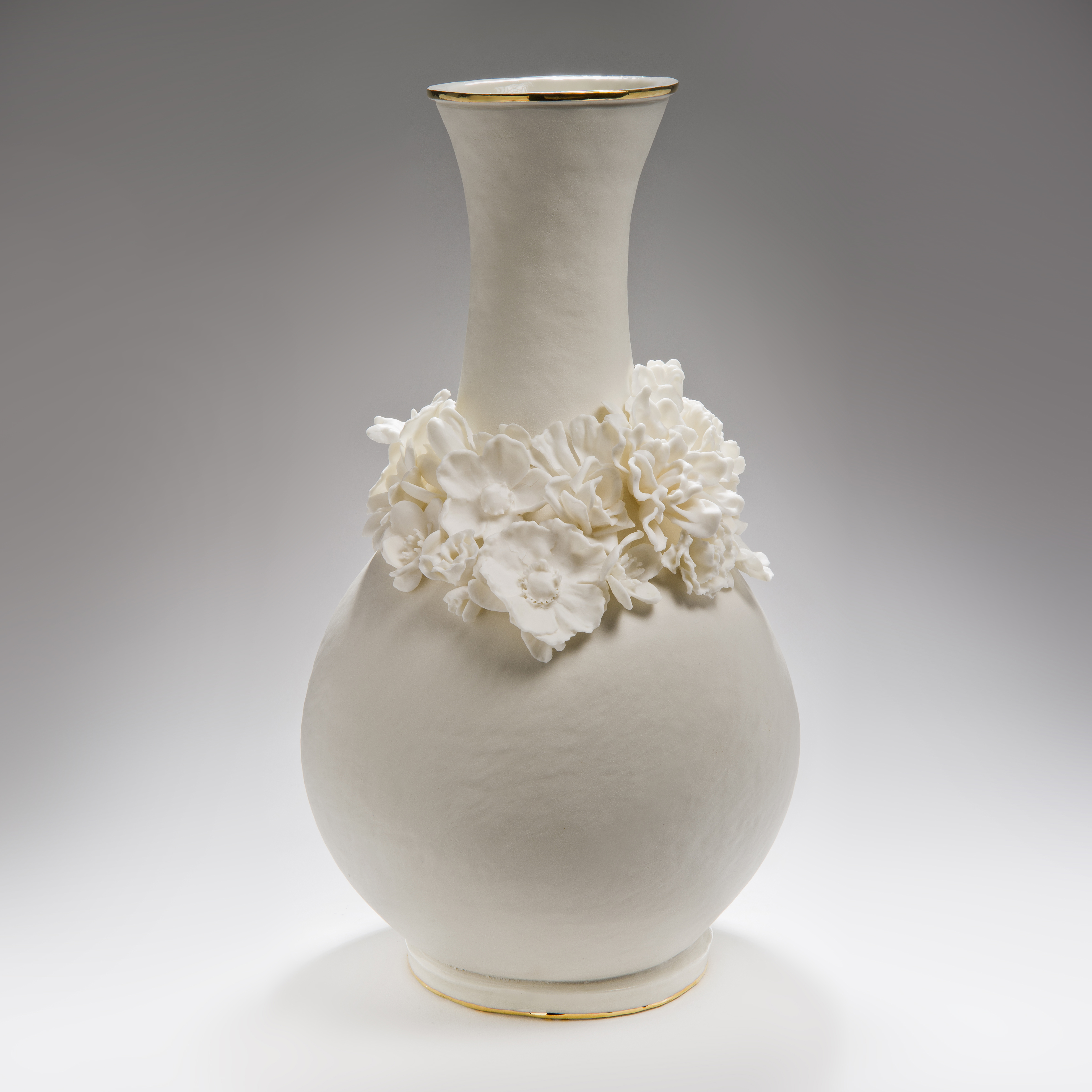 white ceramic vase with wide base and long neck and sculpted flowers